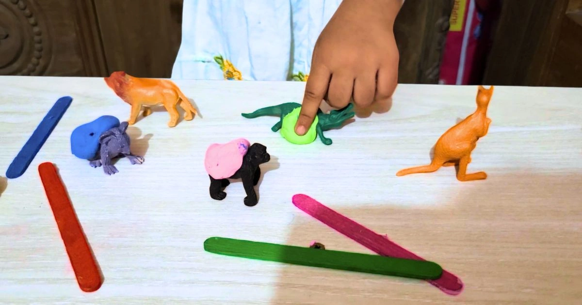 a toddler is playing with animal toys, play dough and popsicle sticks