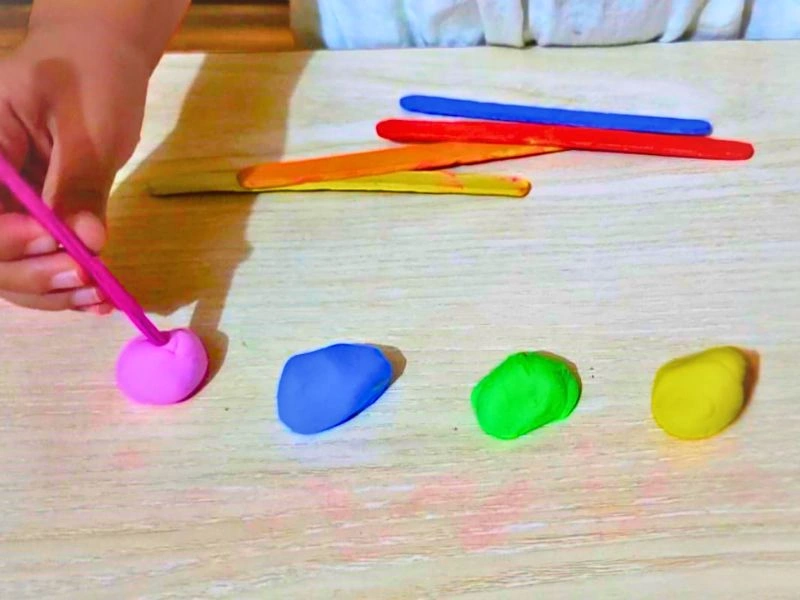 a toddler is sorting colors with playdough and popsicle sticks