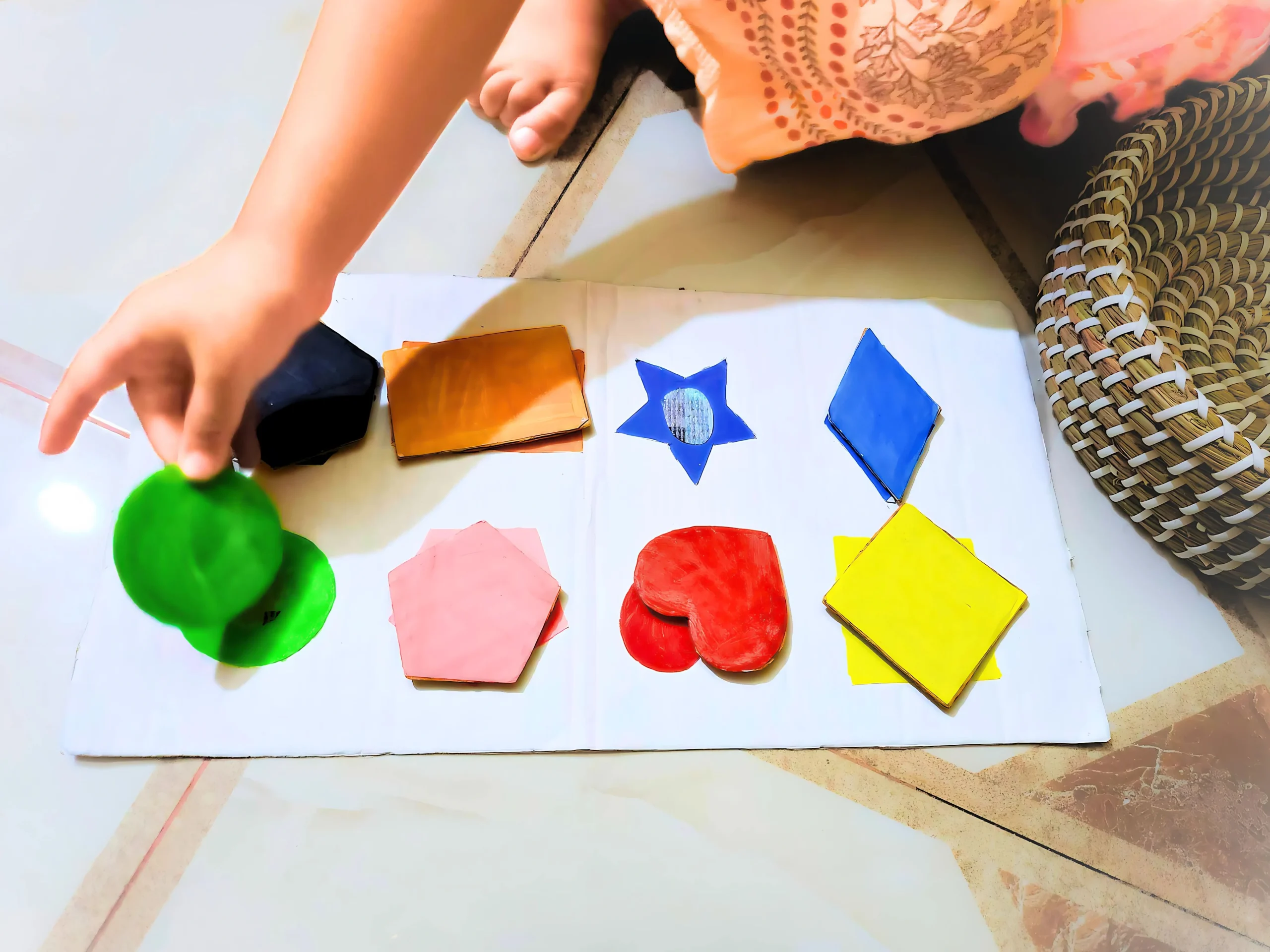 Toddler practicing fine motor skills by sorting shapes on a cardboard with cutout shapes