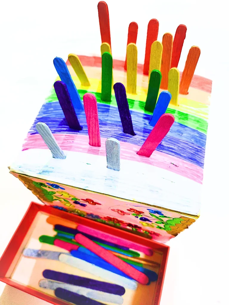 a rainbow patterned DIY color sorting cardboard box where popsicle sticks are posted