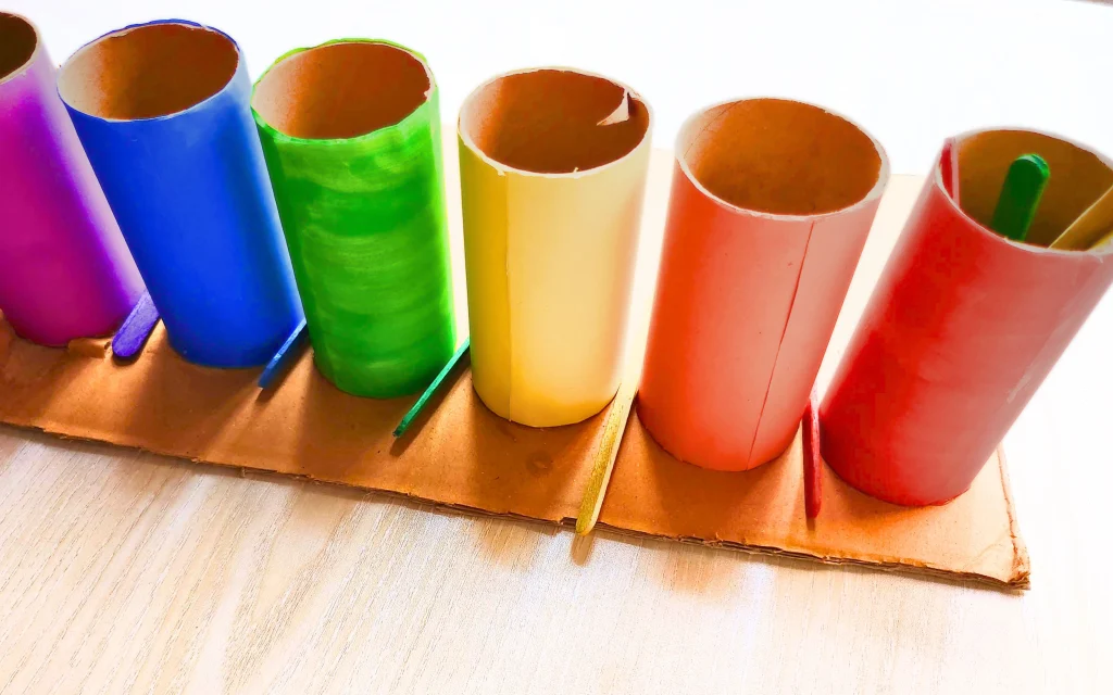colored popsicle sticks are inserted through the gap of the diy toilet paper roll color sorting activity tray