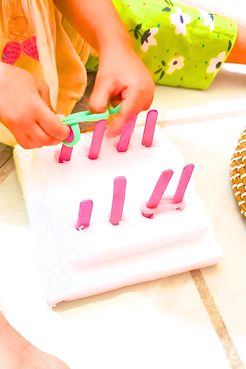 a toddler is looping rubber bands in the DIY geoboard's popsicle pegs