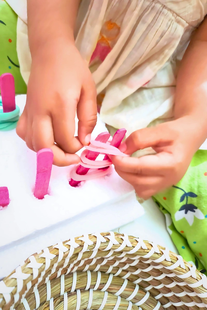 toddler looping elastic band into the popsicle pegs