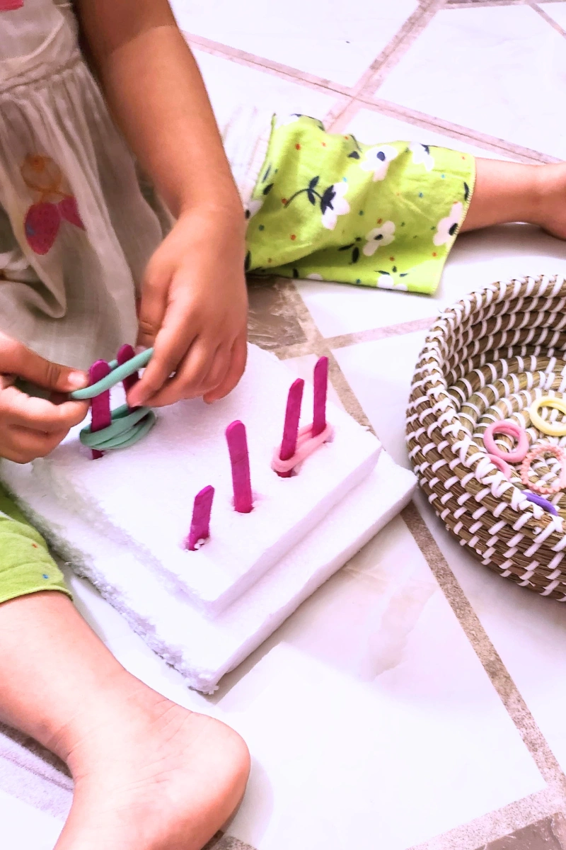 a toddler looping elastic bands into popsicle stick pegs
